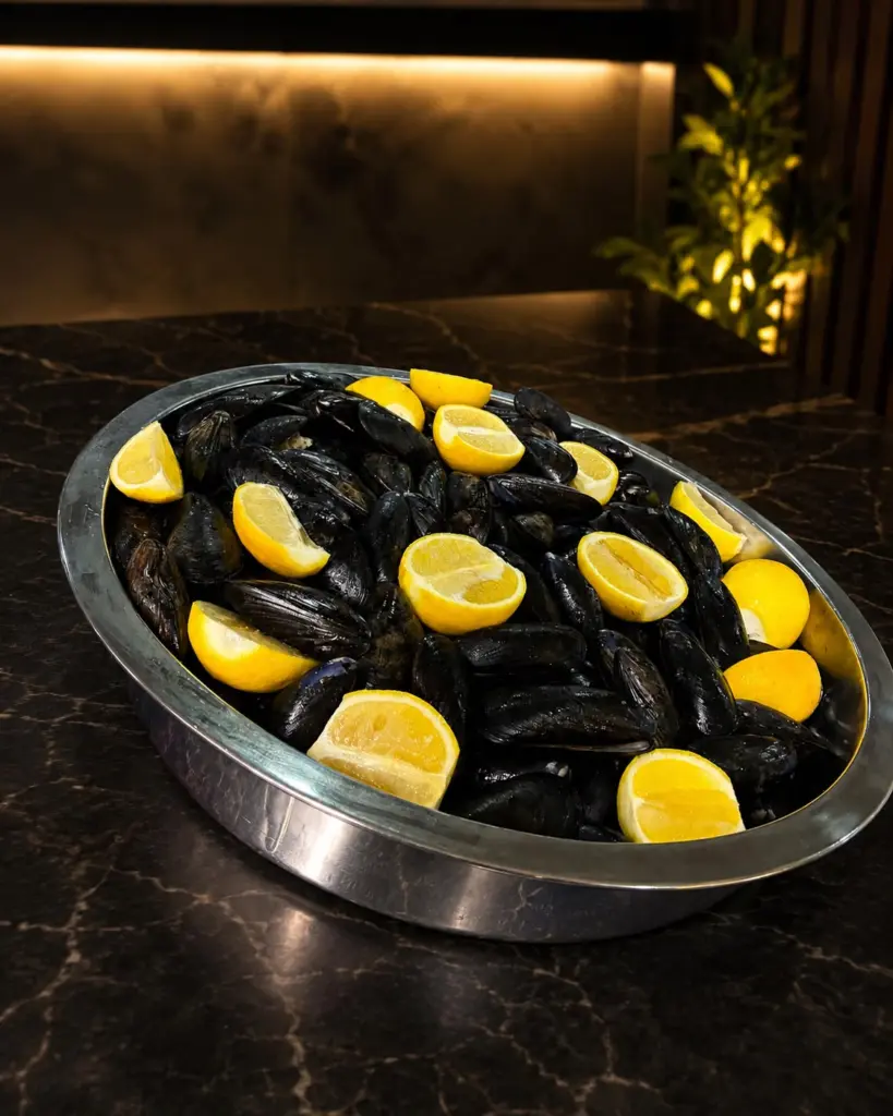 Midye dolma: closed mussel shells stuffed with spiced rice on a steel tray with lemon wedges